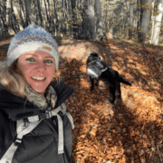 une femme se promène dans la forêt avec son chien qui porte le sac de bât Decathlon