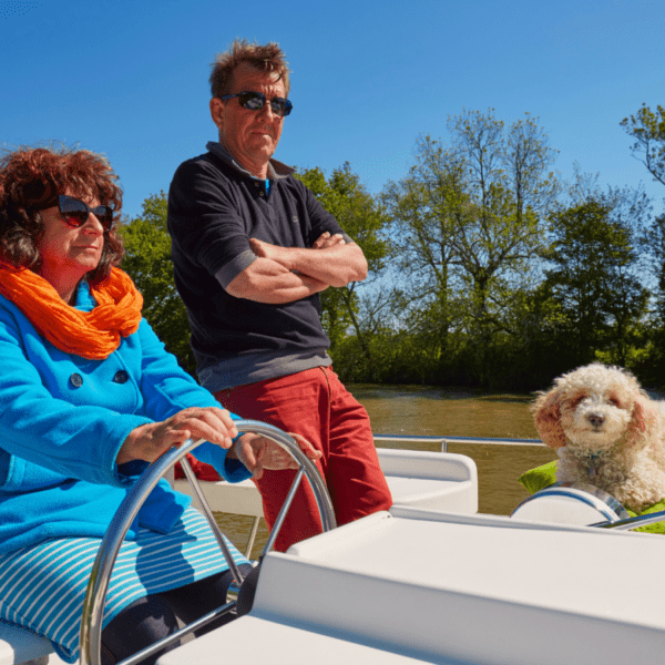 deux personnes et leur chien conduisent leur Pénichette® sur le canal de Nantes à Brest en Bretagne