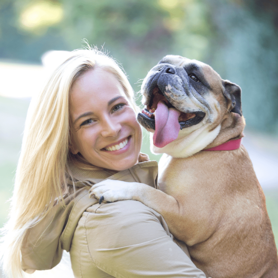 une femme blonde porte son chien bouledogue dans ses bras