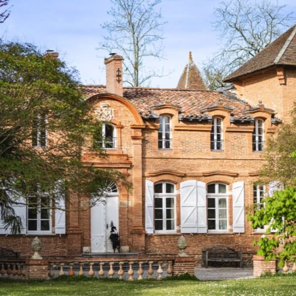 La façade du Gîte la Ferme du Château à Marquefave en Haute-Garonne en Occitanie, avec le berger australien de la propriété, Tim, qui se tient debout sur la porte d'entrée