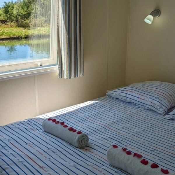 Chambre lit double, avec vue sur le canal de Bourgogne, avec des serviette de bains roulée, avec des pétales de roses dessus du Cottage flottant insolite à Saint-Jean-de-Losne en Côte d'Or en Bourgogne-Franche-Comté