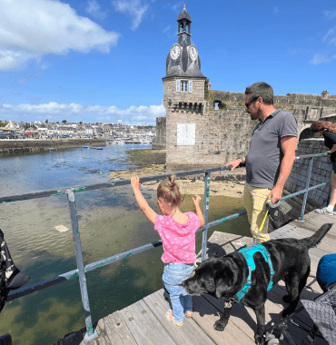 une petite fille et son père qui tient le chien regardent la mer sur la muraille de Concarneau en Bretagne