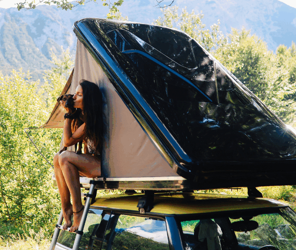 voiture avec tente de toit avec une femme et un chien en voyage