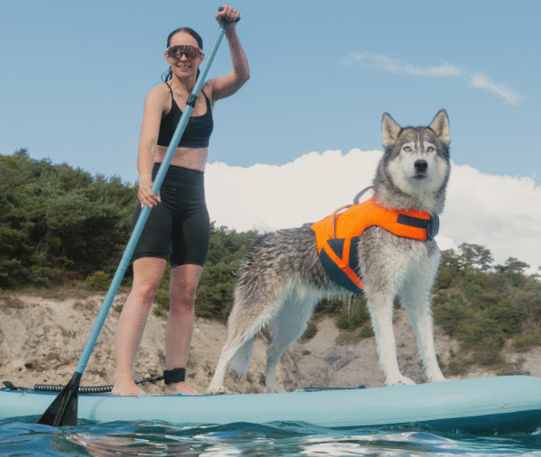 Una donna pratica paddleboard con il suo cane husky, indossando un giubbotto di salvataggio Decathlon.